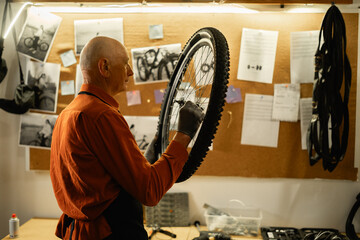 Old man Cycling mechanic checking bicycle wheel in authentic workshop. Garage interior with tools....