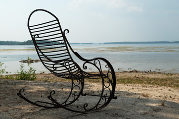 Vintage wrought iron rocking chair on serene lake shore for relaxation.