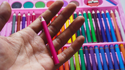 Hand holding one yellow colored pencils with neatly arranged group of colorful pencils background....