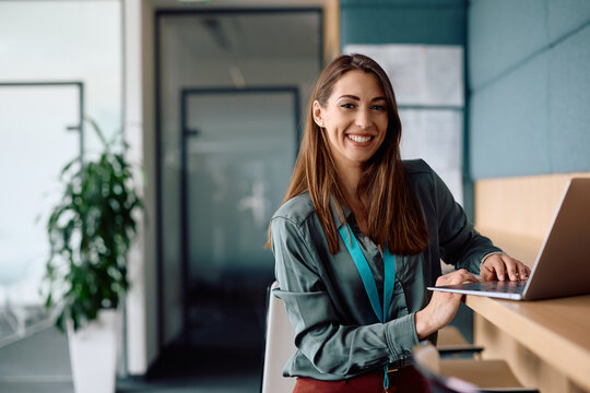 Portrait of happy businesswoman working on laptop  computer in office and looking at camera.