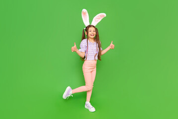 A charming little girl dressed up as an Easter bunny is enjoying the Easter holiday. A full-length child with rabbit ears on his head. Green isolated background. Copy space.