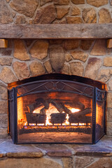 Vertical image of a large stone gas fireplace with a roaring fire and a large natural wooden mantel