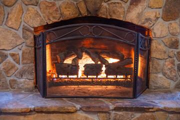 Horizontal view of a large stone gas fireplace with a warm comfortable fire.