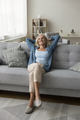 Relaxed elderly woman sit on cozy sofa in living room, enjoy retired life, resting at home alone,...