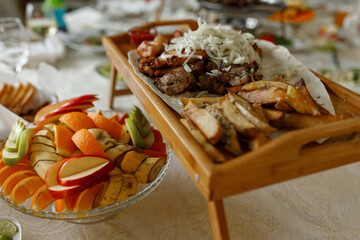 Shish kebab, potatoes and lavash on a wooden board. apples, bananas and orange on a plate