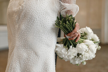 The bride in a white dress holds a bouquet in her hand