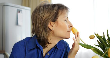 Middle-aged woman inhales yellow tulip scent. Flower fragrance, natural aromatherapy moment, Gen X....