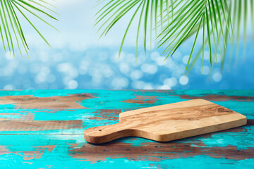 Empty wooden table with cutting board over tropical beach with palm leaves bokeh background.  Summer mock up for design and product display.