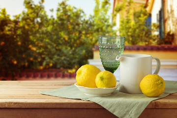 Mediterranean summer concept.  Lemons and white jug on wooden picnic table over lemon tree background - 783845417
