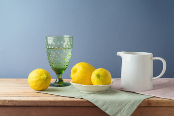 Summer composition with lemons and white jug on kitchen wooden table - 783845426