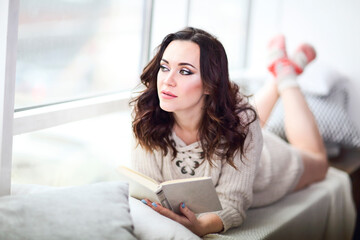 Young beautiful brunette woman  wearing knitted sweater reading book relaxing by the window