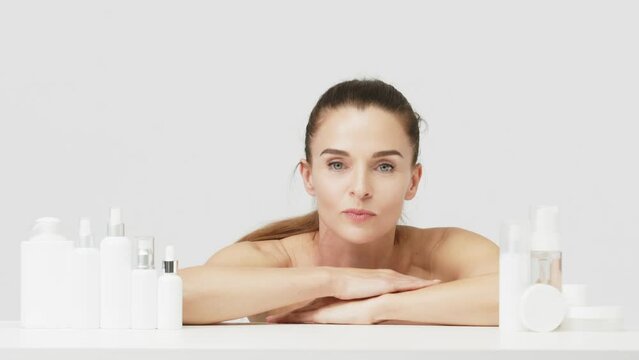 Portrait of a happy attractive middle-aged woman next to mock-ups of jars with cream and cosmetology natural cosmetics. Advertising of spa treatments, anti-aging care products for delicate dry skin.