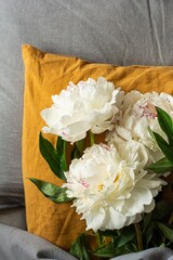 Fresh flowers on the bed (pillow) in the room. Fashionable colors in textiles are gray and terracotta (orange). The concept of restful sleep in clean fragrant bed. Beautiful peonies, present.