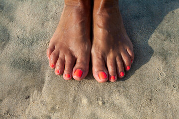 Coastal Comfort: Feet Adorned in Orange Nail Polish on Dry Sand