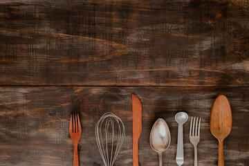Cropped organized set of cutlery side by side on dark weatherd wood background with space for text