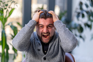 close-up of a young guy office worker against the background of a window sitting on chair with a tablet being angry