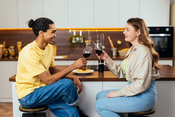 Modern multiethnic unstereotyped couple lifestyle moments at home. Not stereotyped boyfriend and girlfriend living together. Handsome young man and beautiful girl drinking wine and toasting glasses.