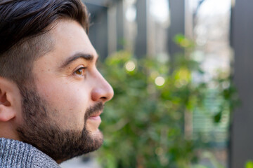 close-up of young guy with a beard thoughtfully looks out the window among the plants