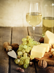 Bottles and glass of white wine, cheese, nuts and grapes