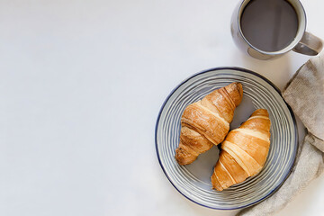 A plate of croissants sits on a table next to a mug of coffee. The croissants are golden brown and appear to be freshly baked
