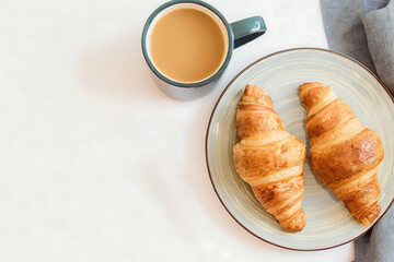 A plate of croissants sits on a table next to a cup of coffee. The croissants are golden brown and appear to be freshly baked