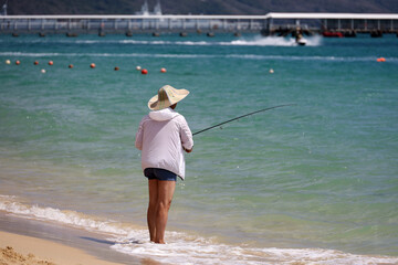 Fisherman in sun hat standing with a fishing rod on a sea beach