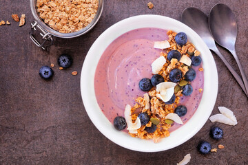 Healthy blueberry and coconut smoothie bowl with granola. Top down view on a dark stone background. - 783869065