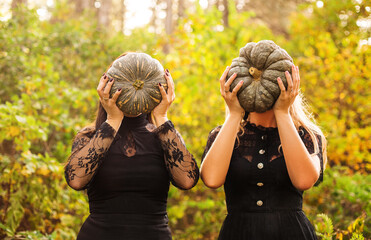 Two female friends holding scary green pumpkins in front of her face