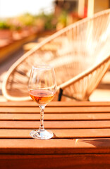 Glass of white wine on rustic wooden table and flower pots on terrace outside