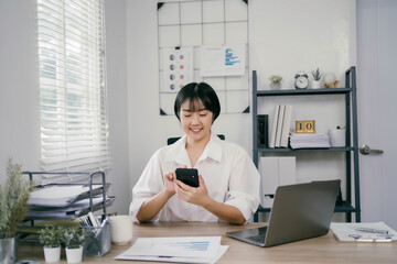 A woman is sitting at a desk with a laptop and a cell phone