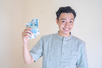 Moslem Asian man happy, smiling when got THR money Ramadan celebration. The photo is suitable to use for Ramadhan poster and Muslim content media.