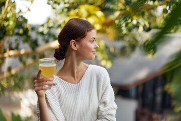 Woman holding a glass of refreshing kombucha outdoors in the sunlight, enjoying a healthy and relaxing moment surrounded by nature The vibrant green scenery adds to the feeling of freshness, while the