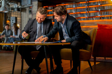 in the office the director sits with business partner discussing a deal and signing documents