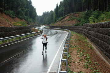 Young woman with yellow backpack walking on wet road among mountains. Female tourist spending...