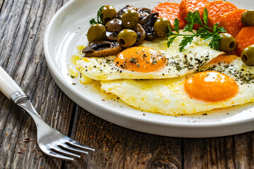 Breakfast - sunny side up egg, toasted bread, sweet potato, mushrooms  and olives served on wooden table
