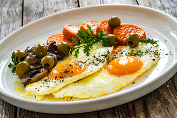 Breakfast - sunny side up egg, toasted bread, sweet potato, mushrooms  and olives served on wooden table
