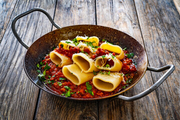 Paccheri con ragù alla bolognese - noodles with bolognese sauce on frying pan on wooden table
