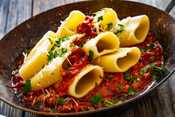 Paccheri con ragù alla bolognese - noodles with bolognese sauce on frying pan on wooden table
