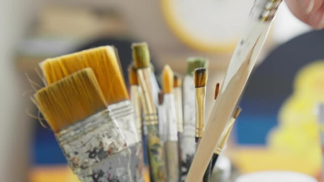 Artist picks up paint brush. Female artist hand picking up brush for painting. Unrecognizable young artist choosing brushes. Close-up in 4K, UHD