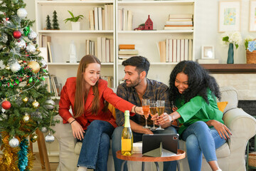 Group of young adults having a festive time, engaging with technology and enjoying drinks by a decorated Christmas tree in a cozy setting.