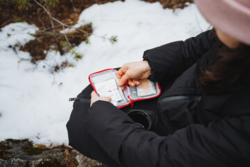 Woman taking pills from a small red first aid kit while sitting in the forest on the background of...