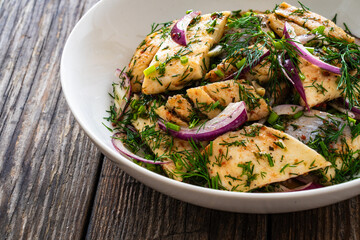 Marinated herring fillets with dill and red onion on wooden table
