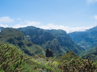 View of green hills, mountain landscape in clouds at blue sky. and lush vegetation at hiking trail PR12 to Pico Grande one of the highest peaks in the Madeira, Portugal