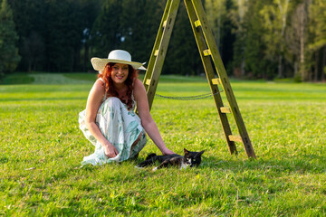 woman on a meadow with a ladder stroking a cat