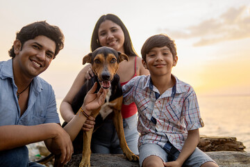 Happy Family Enjoying Sunset With Their Dog At Beach