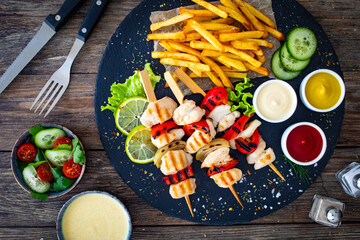 Meat skewers - grilled meat with French fries and fresh  vegetables on wooden background
