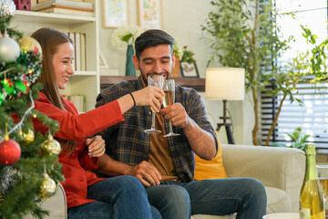 Amidst holiday decorations, a couple shares a cheerful toast with flutes of bubbly, reveling in the...