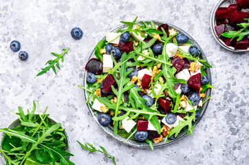 Healthy useful salad with beetroot, blueberries, feta cheese, arugula and walnuts, gray table background, top view - 783906239