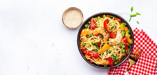 Spicy stir fry noodles with shrimps, colorful paprika, green pea, green onion and sesame seeds with ginger, garlic and soy sauce. White table background, top view banner