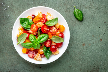 Simple italian salad with with stale bread, cherry tomatoes, olive oil, sea salt and green basil white plate, stone table background, top view - 783906453